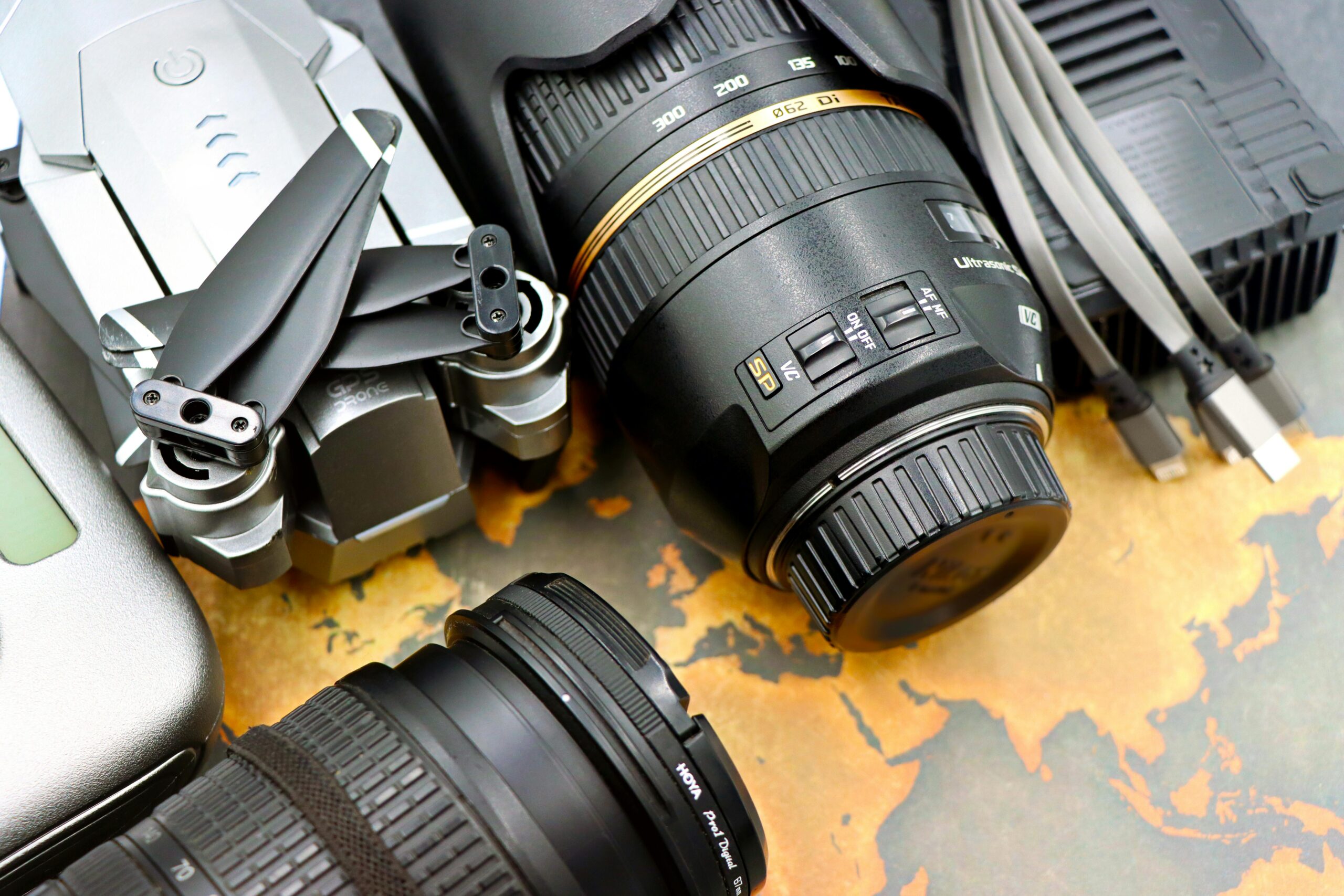 Top view of photography equipment including drone, camera lenses, and USB cables on map background.